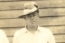 A sepia photo of a police officer wearing a slouch hat, standing in front of a weatherboard building.