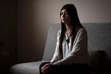 Young woman sits on a sofa inside home.