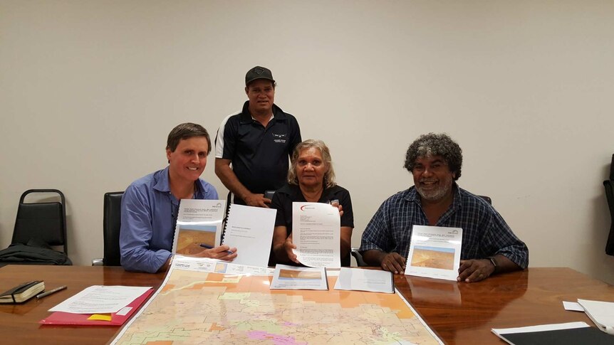 Four traditional owners sit with mining executive signing a mining agreement