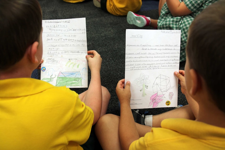 Two students hold letters they have written to pen pals about their hobbies, family and school life.