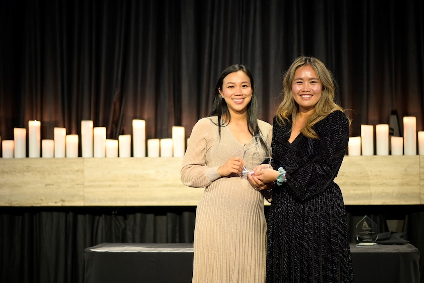 Two women hold an award trophy.