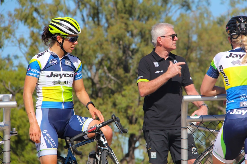 A man in a black shirt points while two female cyclists listen on.