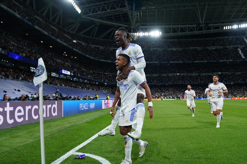 A Real Madrid player roars in celebration of a goal at the corner flag as he carries a teammate on his shoulders.