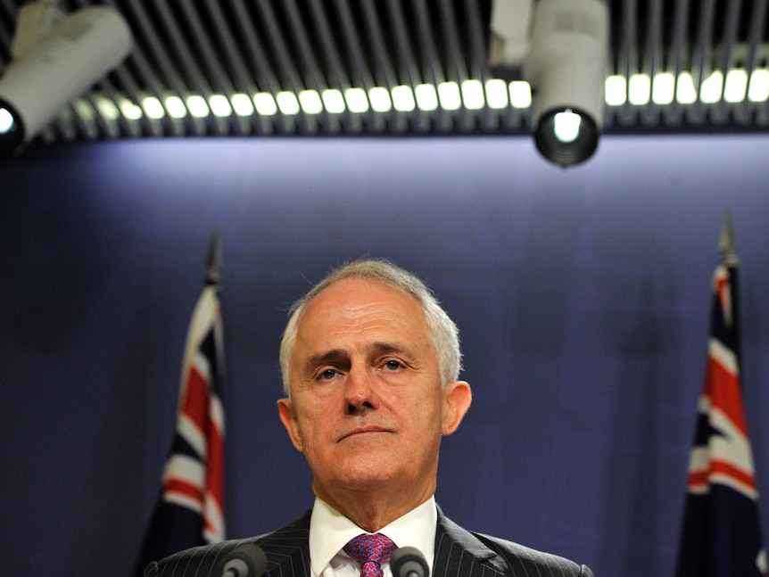 Prime Minister Malcolm Turnbull stands in front of Australian flags addressing the media.