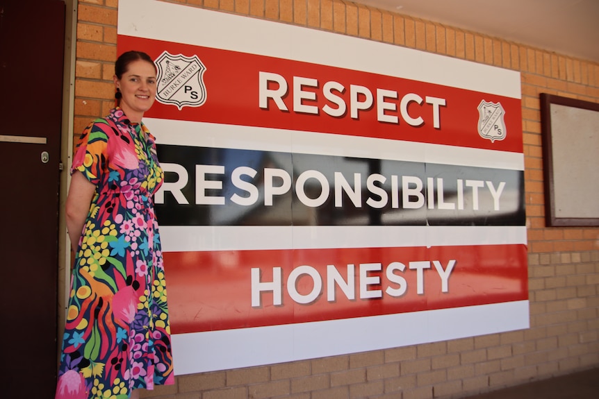 A woman in a colourful dress standing next to a school sign with the words 'respect, responsibility, honesty'
