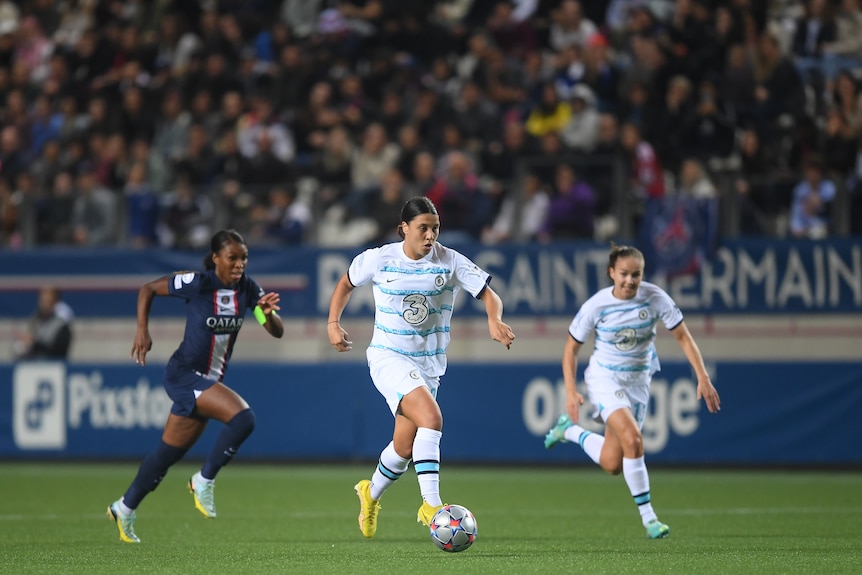 Sam Kerr runs with the ball as a PSG opponent and Chelsea teammate follow her.