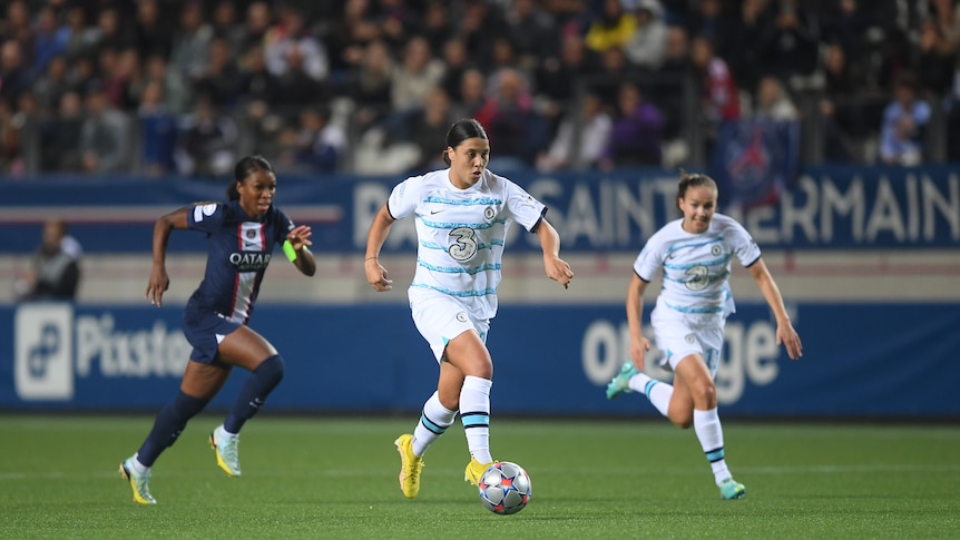 Sam Kerr runs with the ball as a PSG opponent and Chelsea teammate follow her.