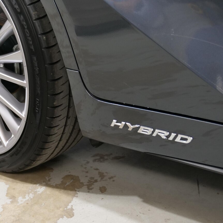 A close shot of the side of a car, featuring the word hybrid written in silver