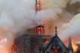 The burning spire of a gothic cathedral glows orange as smoke billows from it.