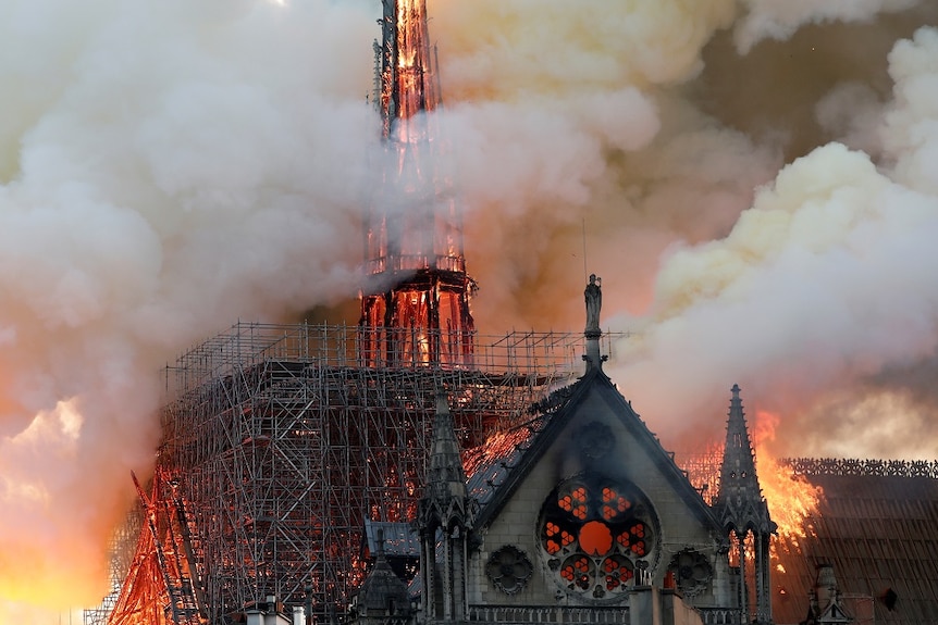 The burning spire of a gothic cathedral glows orange as smoke billows from it.