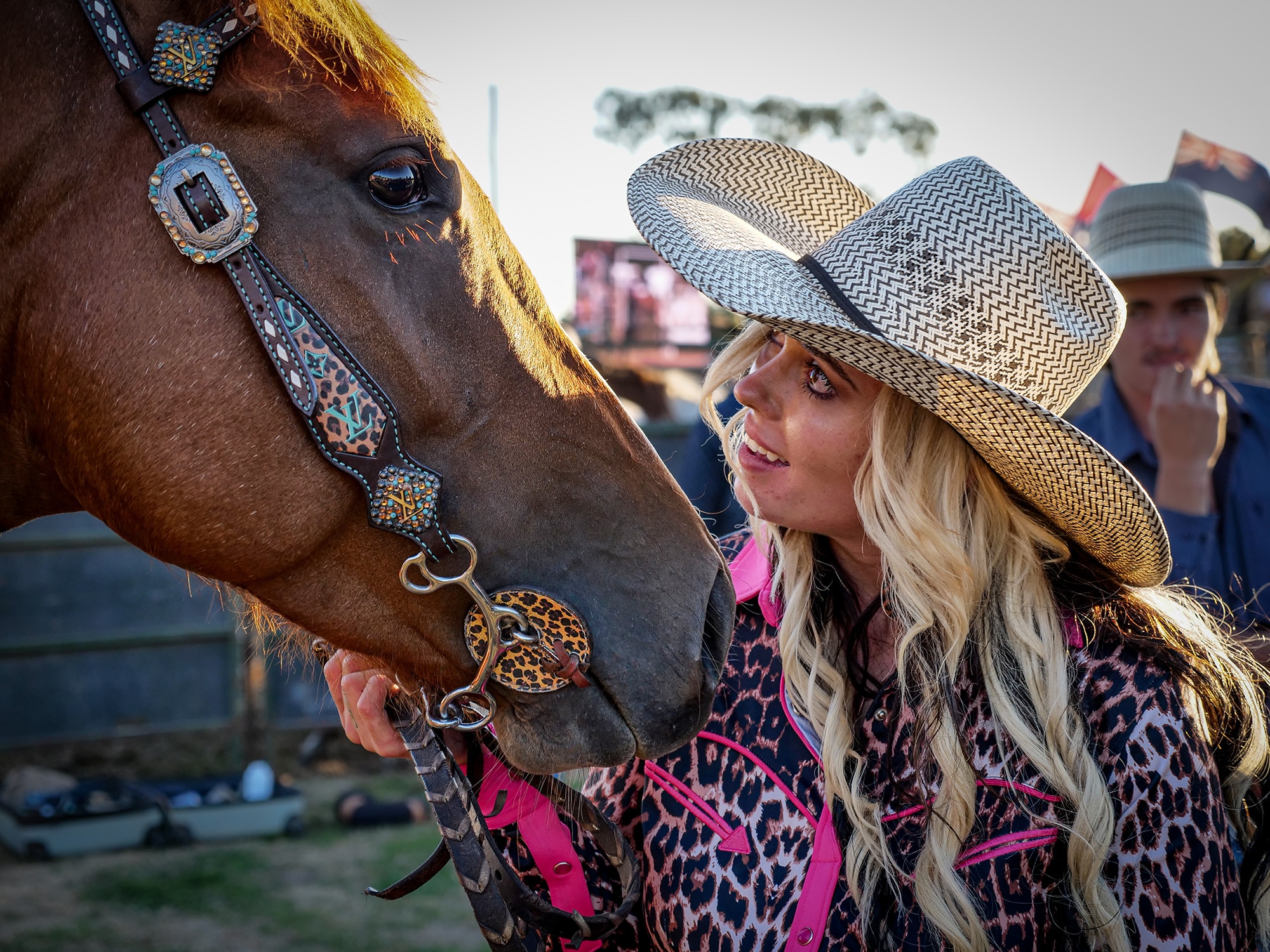 A woman wearing a cowboy hat looks fondly at a chestnut horse