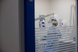 Looking through the door of a dental clinic where a dentist inside prepares a chair and equipment.