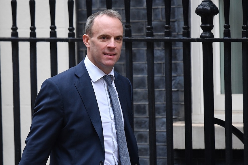 Britain's Foreign Secretary and First Secretary of State Dominic Raab in a suit walking on a street.