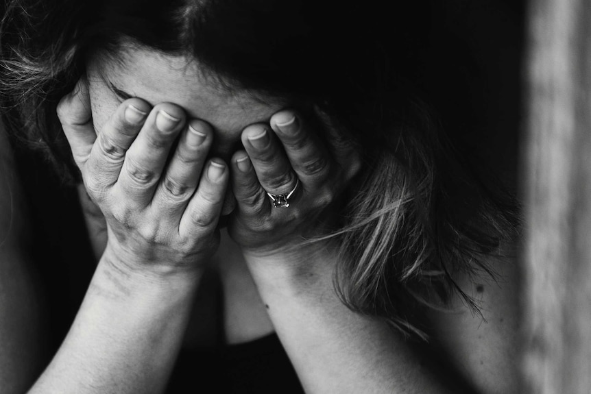 A black and white image of a worried woman with hands over her face.