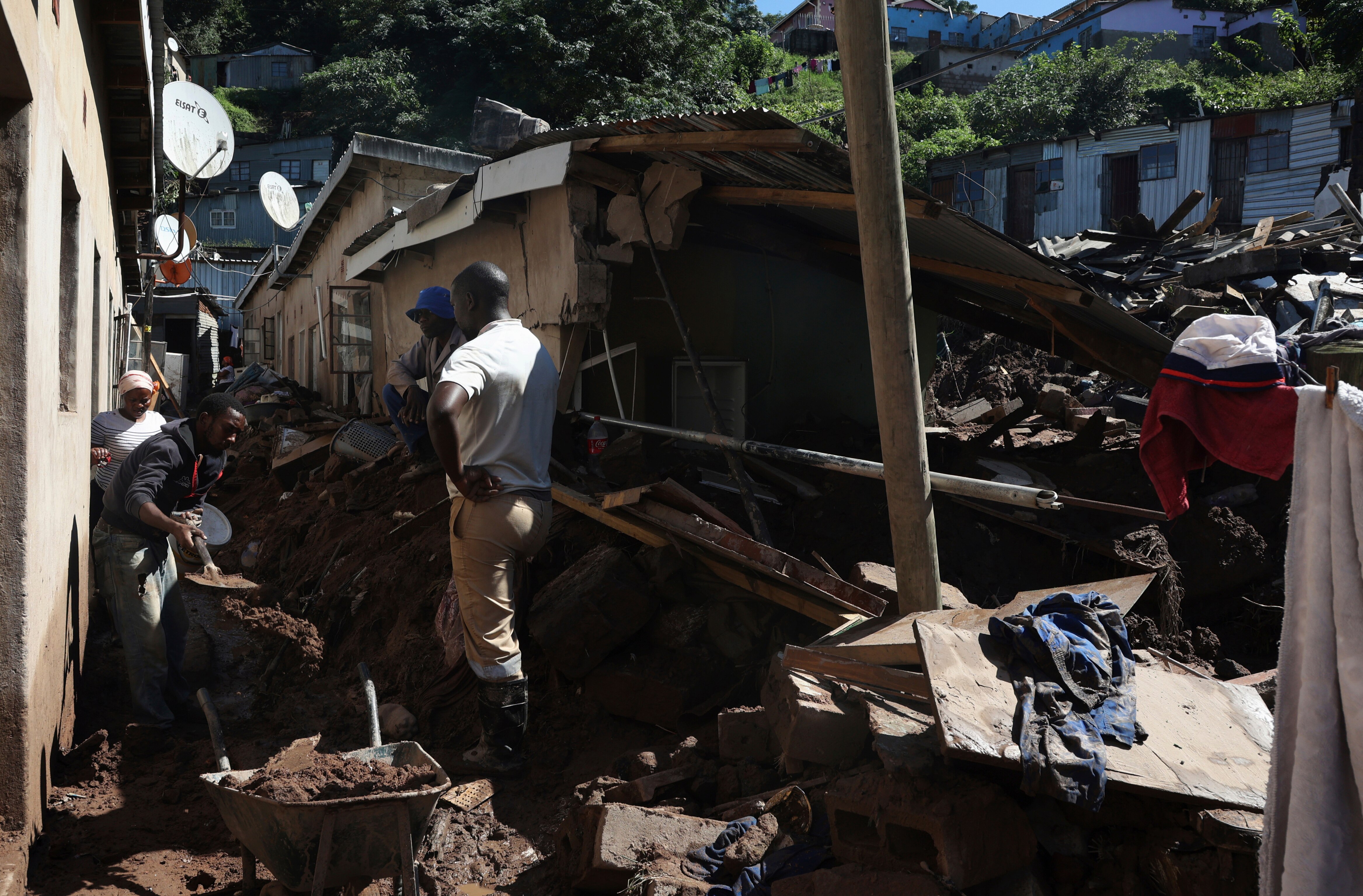 People standing near damaged houses, shovelling mud into wheelbarrows.