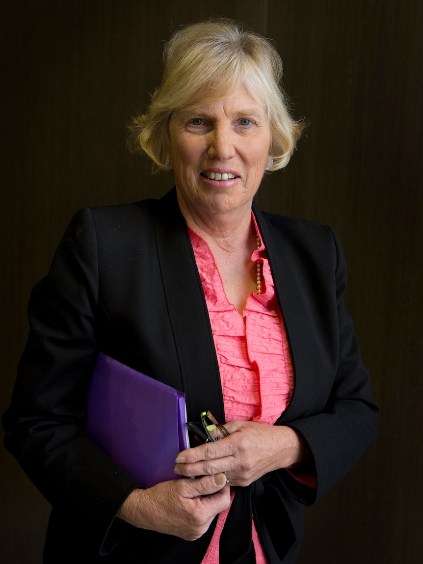 A woman with short hair stands holding a folder.