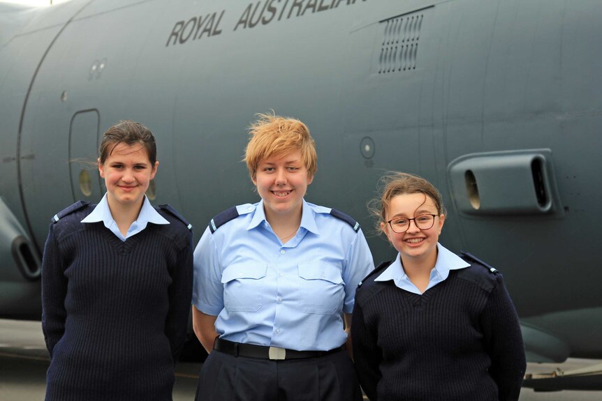 Three young women in air force cadet uniforms in front of a grey plane