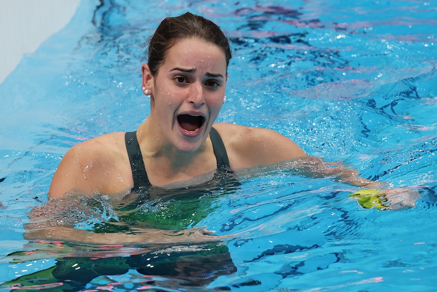 A brunette woman screams while swimming in a pool