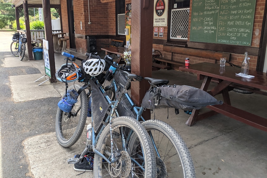 Two bikes are propped up against a post outside a pub entrance.