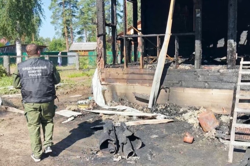 A man with his back to the camera, looking at a burnt home
