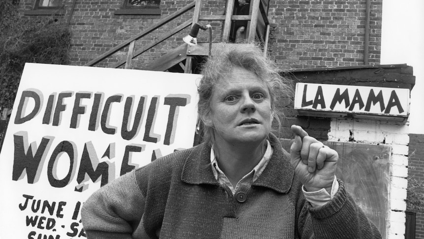 Outside a brick building with signs for 'Difficult Women' and 'La Mama', Liz Jones points at the camera with a fierce expression