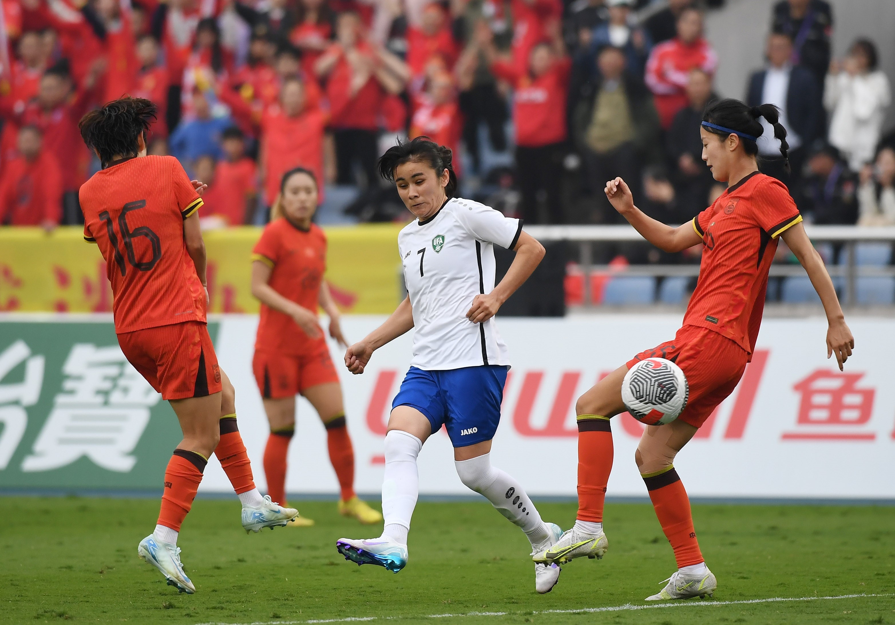 Um membro da seleção feminina de futebol do Uzbequistão passou a bola enquanto dois defensores se aproximavam para atacar.