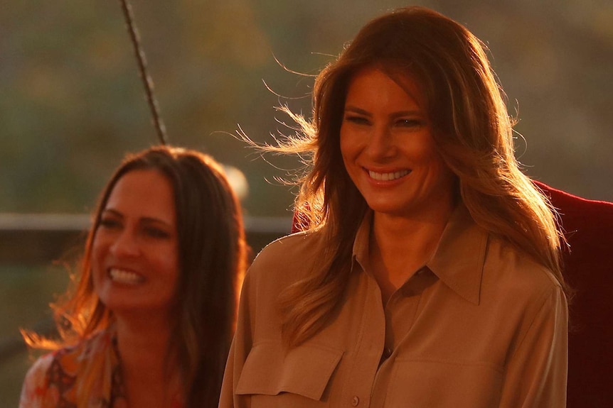 Melania Trump sits next to her Communications Director Stephanie Grisham in orange lighting.