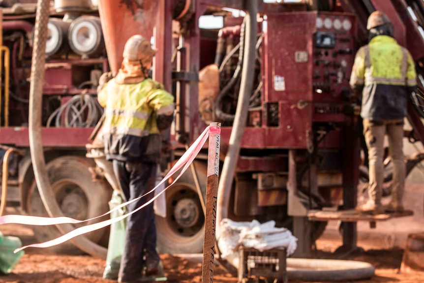 Two men wearing high-vis workwear working on a drill rig in bushland.