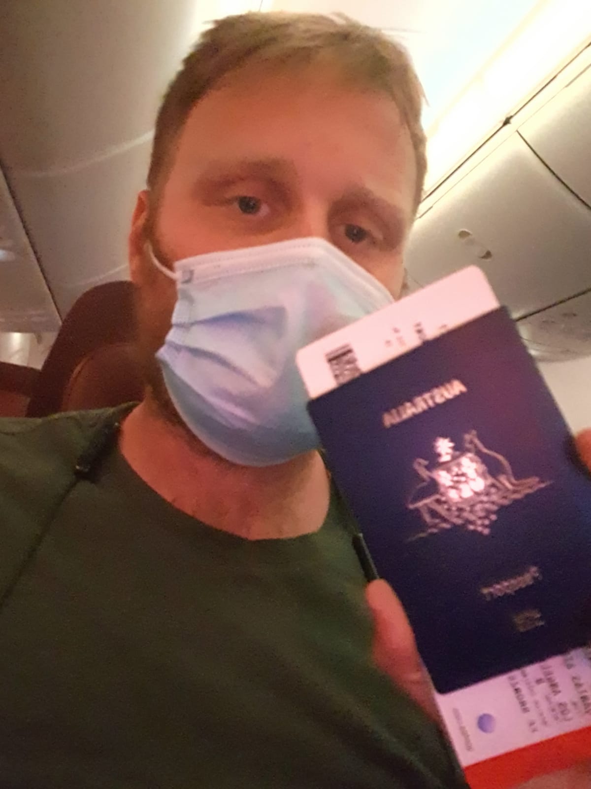 Close-up of a man wearing a face mask holding his passport and boarding pass. 