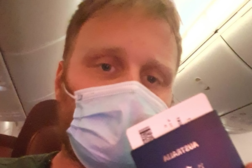 Close-up of a man wearing a face mask holding his passport and boarding pass. 