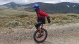 A boy rides a unicycle along a gravel mountain path.