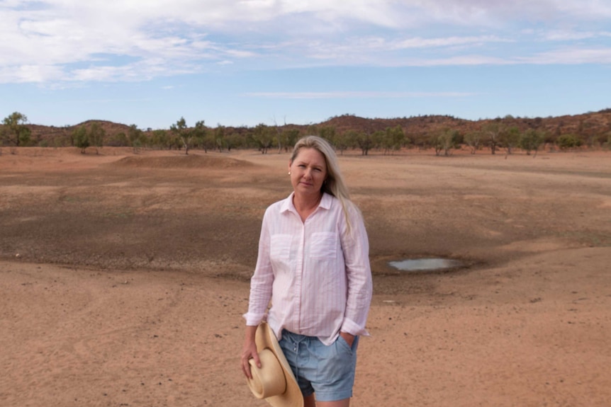 A woman with a hat in her hand next to a dry dam.