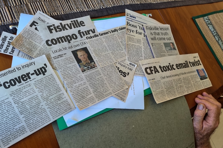 newspaper clippings with headlines about Fiskville are spread across a dining room table.