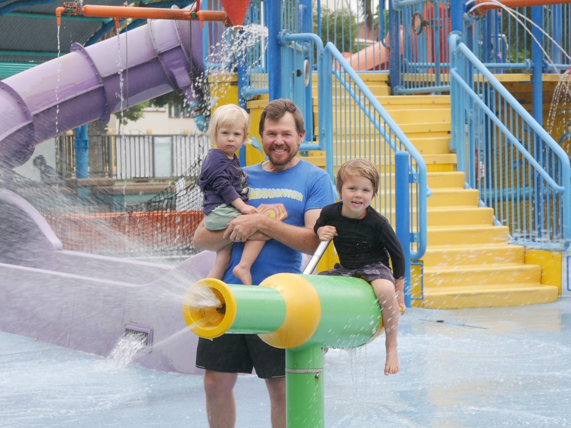 A dad and two young children play on equipment in a waterpark. 