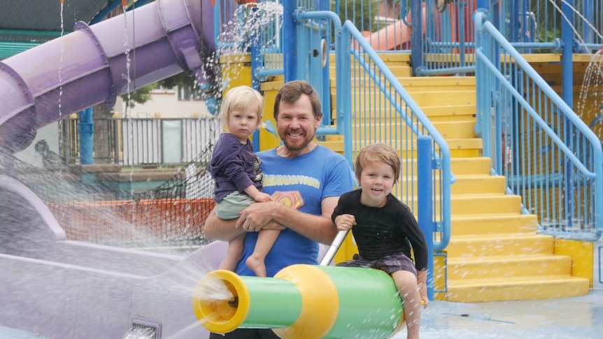 A dad and two young children play on equipment in a waterpark. 