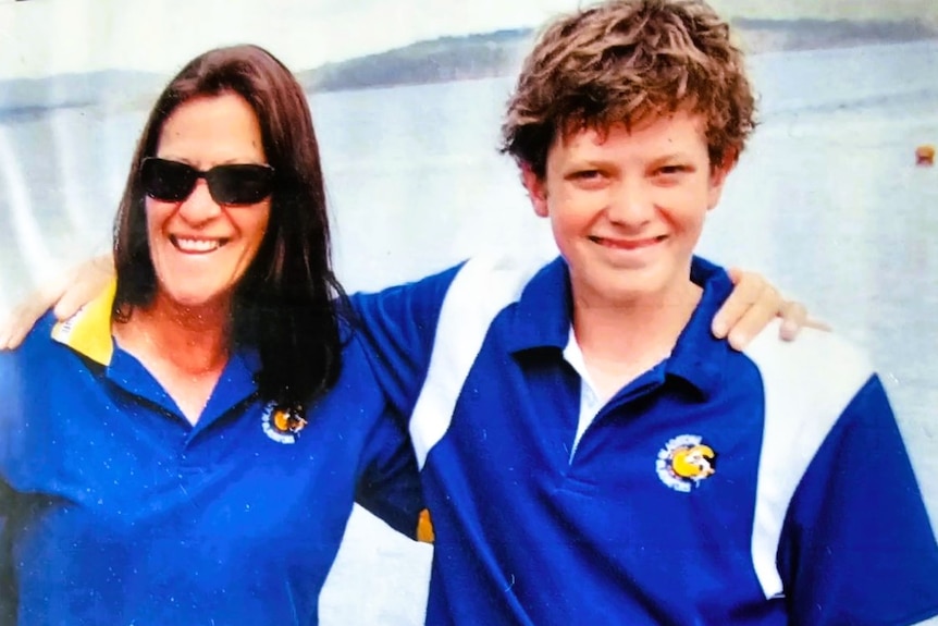 A woman with long dark hair and young boy wearing blue shirts with arms around each other standing near a pool.