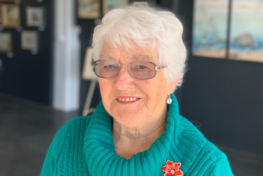 A woman with silver hair and glasses smiles at the camera 