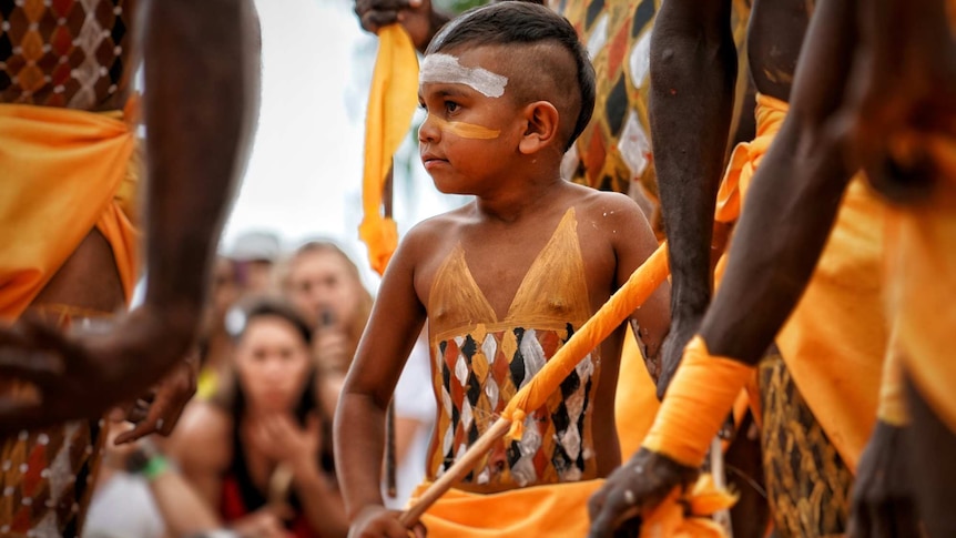 A young Aboriginal boy dances, his body is decorated with traditional pigment markings.