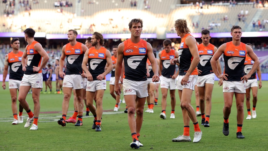 A group of AFL players look around at each other as they wander off the ground.