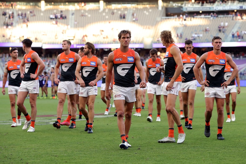 A group of AFL players look around at each other as they wander off the ground.