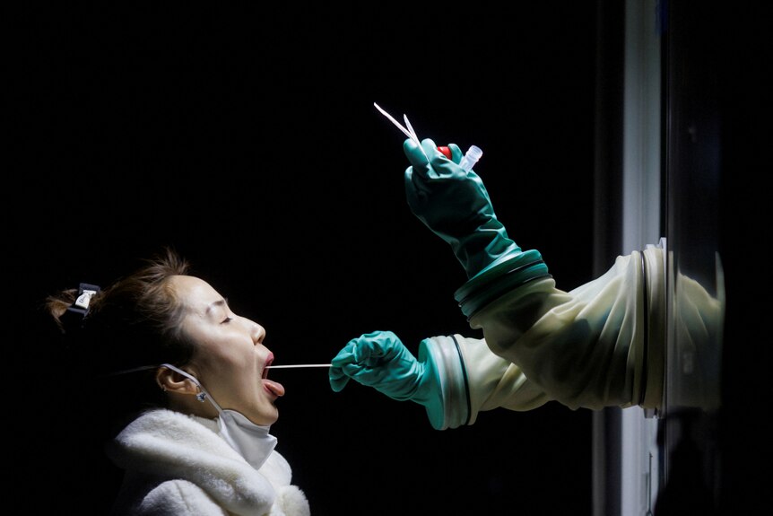 A woman receives a throat swab test at a street booth.