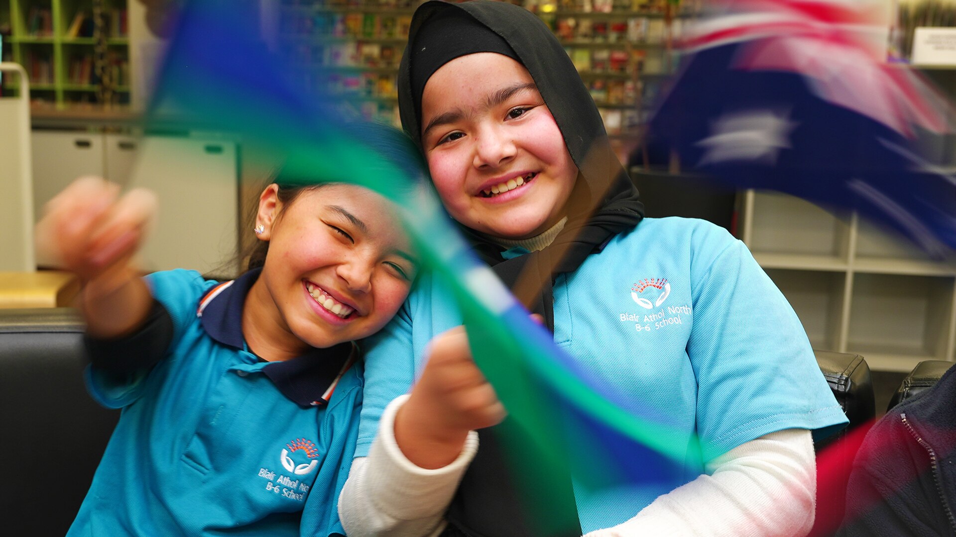 Yasamin and Hadia smile while waving flags, one of which is the Australian flag.