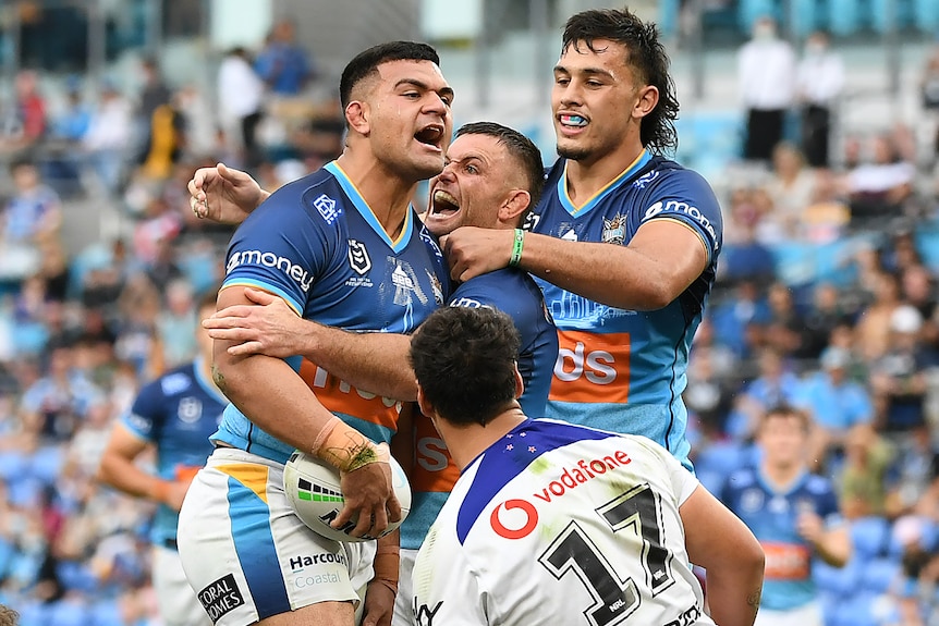 Three Gold Coast Titans NRL players celebrate a try against the Warriors.