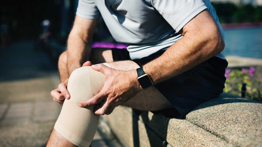 A man holds his knee, which has a compression wrap around it