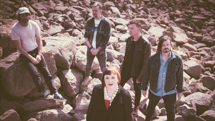 Four men and one woman stand together on the rocks near a body of water