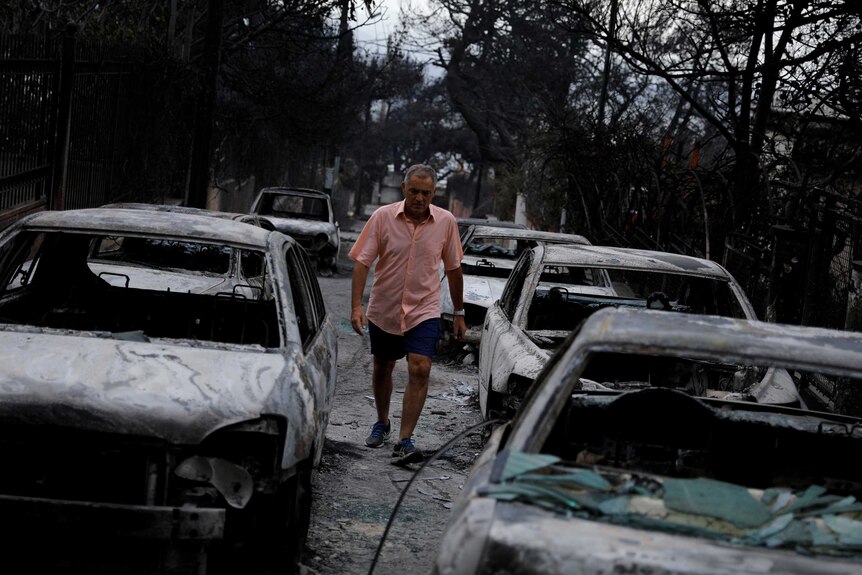 A man walks among burnt cars following a wildfire at the village of Mati.