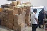 Two men stand near a stack of cardboard boxes.