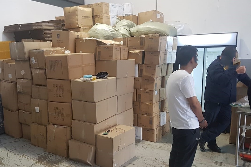 Two men stand near a stack of cardboard boxes.