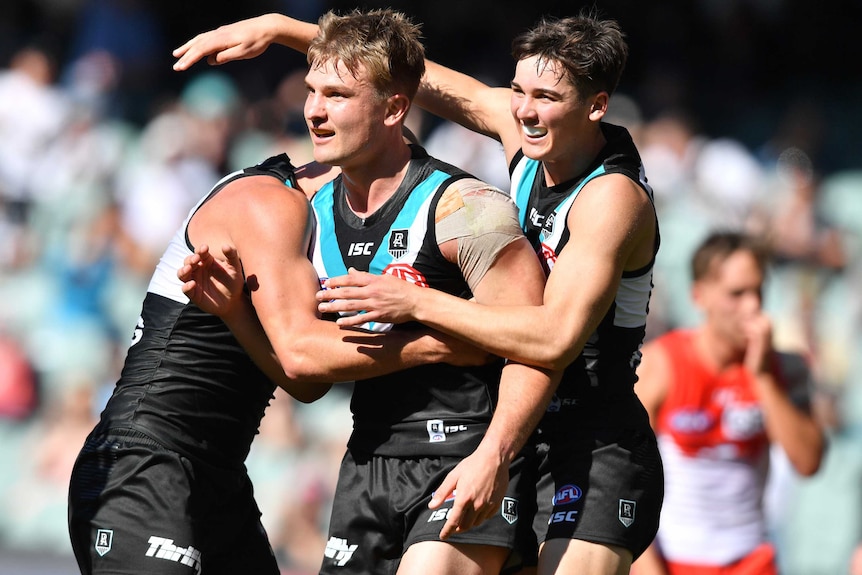 Three Port Adelaide AFL players embrace as they celebrate a goal against the Swans.