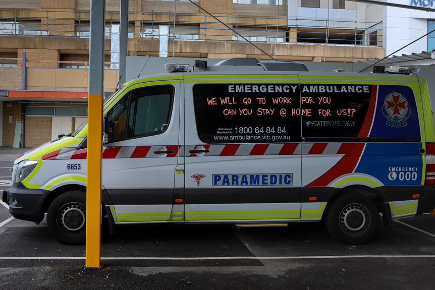 Ambulance in hospital parking lot with message written on window asking for people to practice social distancing